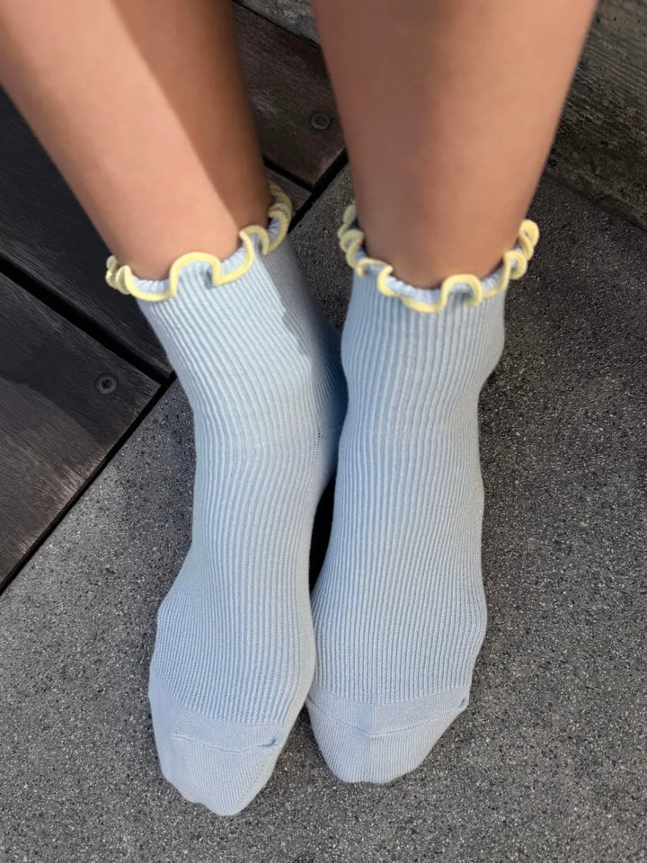 A top-down view shows The Petite Ruffled Modal Socks in Baby Blue / Butter from Le Bon Shoppe being worn against a concrete floor | Twentyseven Toronto