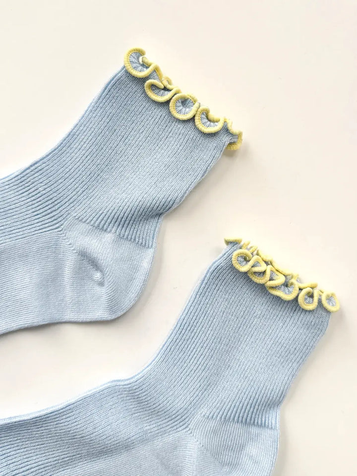 A close-up flat-lay detailing the stitching and contrast yellow trim along the top cuff of The Petite Ruffled Modal Socks in Soft Baby Blue / Butter from Le Bon Shoppe | Twentyseven Toronto