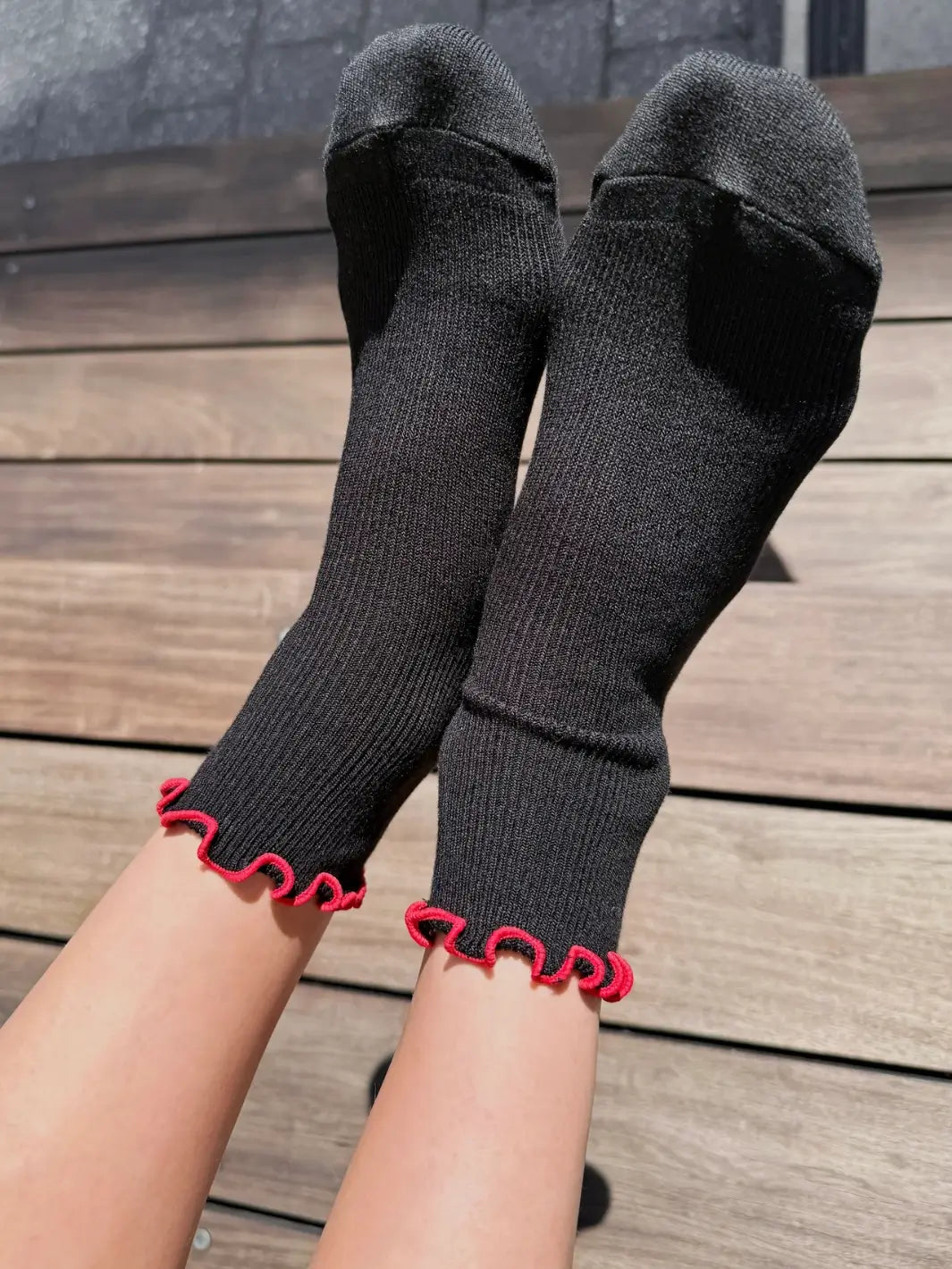 A person wearing a ribbed knit and vibrant red wavy cuffs of The Petite Ruffled Modal Socks in Black / Red from Le Bon Shoppe | Twentyseven Toronto