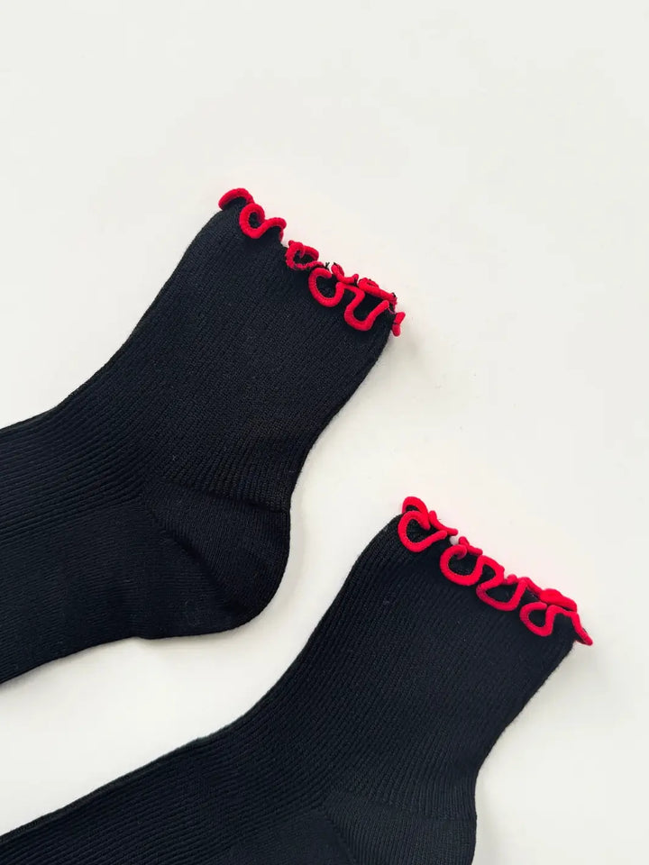 Close up shot of The Petite Ruffled Modal Socks in Black / Red from Le Bon Shoppe to showcase the black body and contrasting red ruffled trim against a plain white background | Twentyseven Toronto