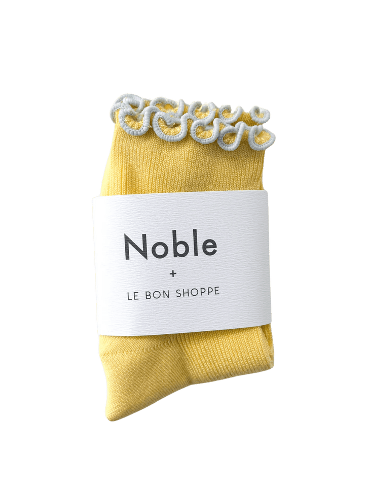 A pair of The Petite Ruffled Modal Socks in Butter / Baby Blue from Le Bon Shoppe is displayed with its white "Noble + LE BON SHOPPE" collaborative packaging band | Twentyseven Toronto