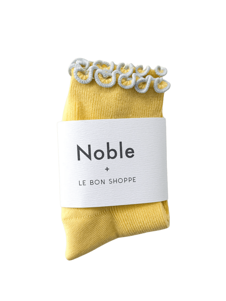A pair of The Petite Ruffled Modal Socks in Butter / Baby Blue from Le Bon Shoppe is displayed with its white "Noble + LE BON SHOPPE" collaborative packaging band | Twentyseven Toronto