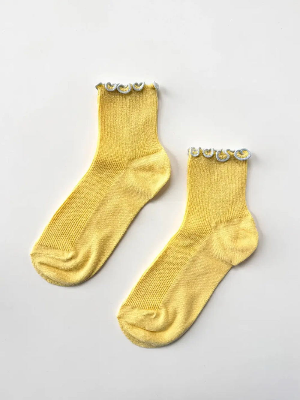 A flat-lay view captures a of pair yellow and baby blue Petite Ruffled Modal Socks in Butter / Baby Blue from Le Bon Shoppe resting on a white background | Twentyseven Toronto