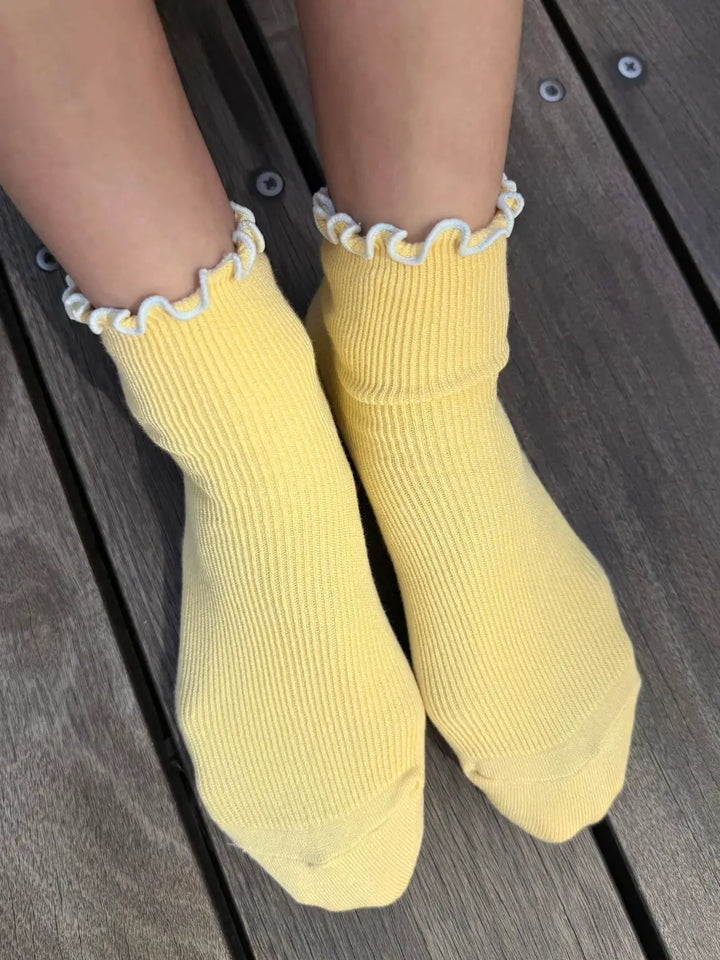 A top-down view shows The Petite Ruffled Modal Socks in Butter / Baby Blue from Le Bon Shoppe being worn resting against a wooden deck | Twentyseven Toronto