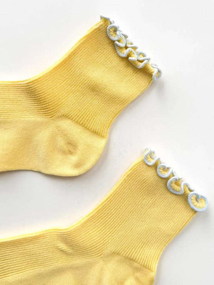 A close-up flat-lay detailing the stitching and contrast blue trim along the top cuff of The Petite Ruffled Modal Socks in Butter / Baby Blue from Le Bon Shoppe | Twentyseven Toronto