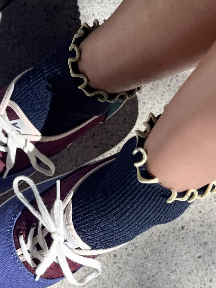 An overhead, close-up shot of a person wearing The Petite Ruffled Modal Socks in Butter / Navy from Le Bon Shoppe highlighting the yellow frilled edges | Twentyseven Toronto
