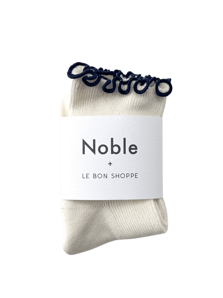 A pair of The Petite Ruffled Modal Socks in Soft White / Navy from Le Bon Shoppe is displayed with its white "Noble + LE BON SHOPPE" collaborative packaging band | Twentyseven Toronto