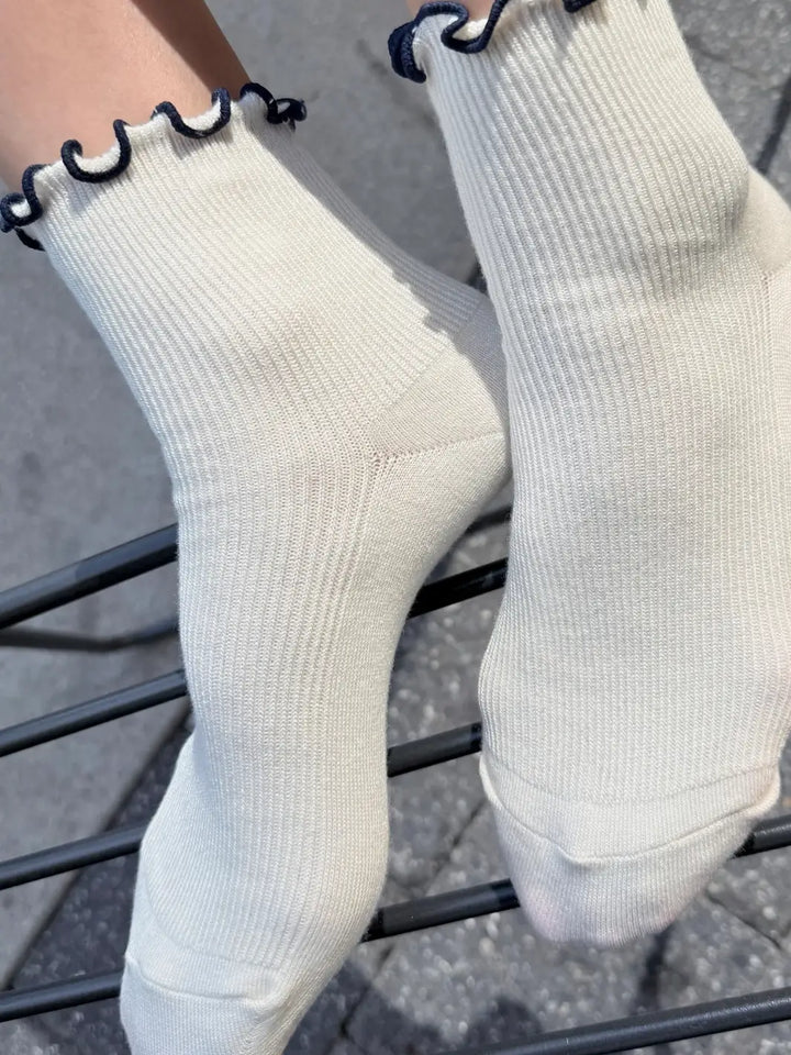 A close-up side view emphasizes the ribbed material and ruffled trim of The Petite Ruffled Modal Socks in Soft White / Navy from Le Bon Shoppe | Twentyseven Toronto