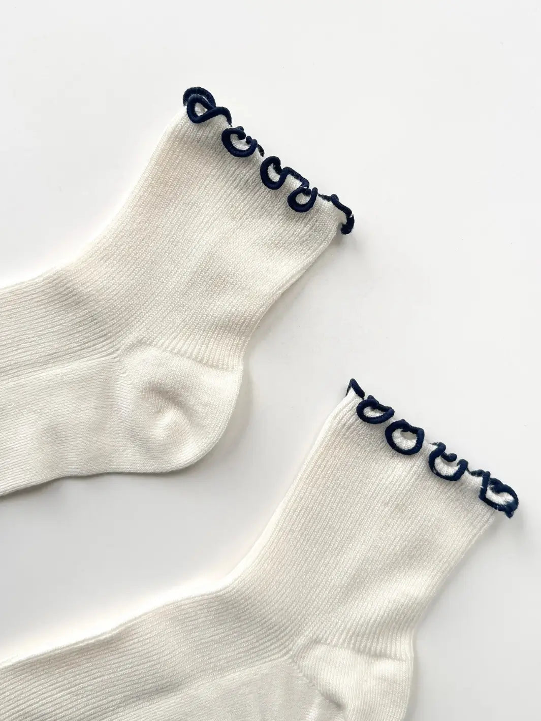 A close-up flat-lay detailing the stitching and contrast navy trim along the top cuff of The Petite Ruffled Modal Socks in Soft White / Navy from Le Bon Shoppe | Twentyseven Toronto