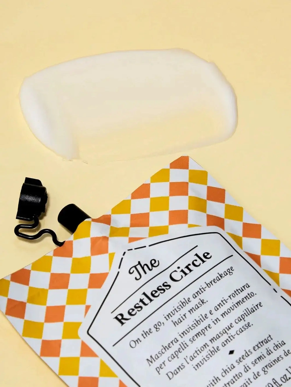 An open pouch of Davines The Restless Circle of Chronicles Hair Mask lies flat on a light yellow background next to a smooth smear of its white cream product | Twentyseven Torotno