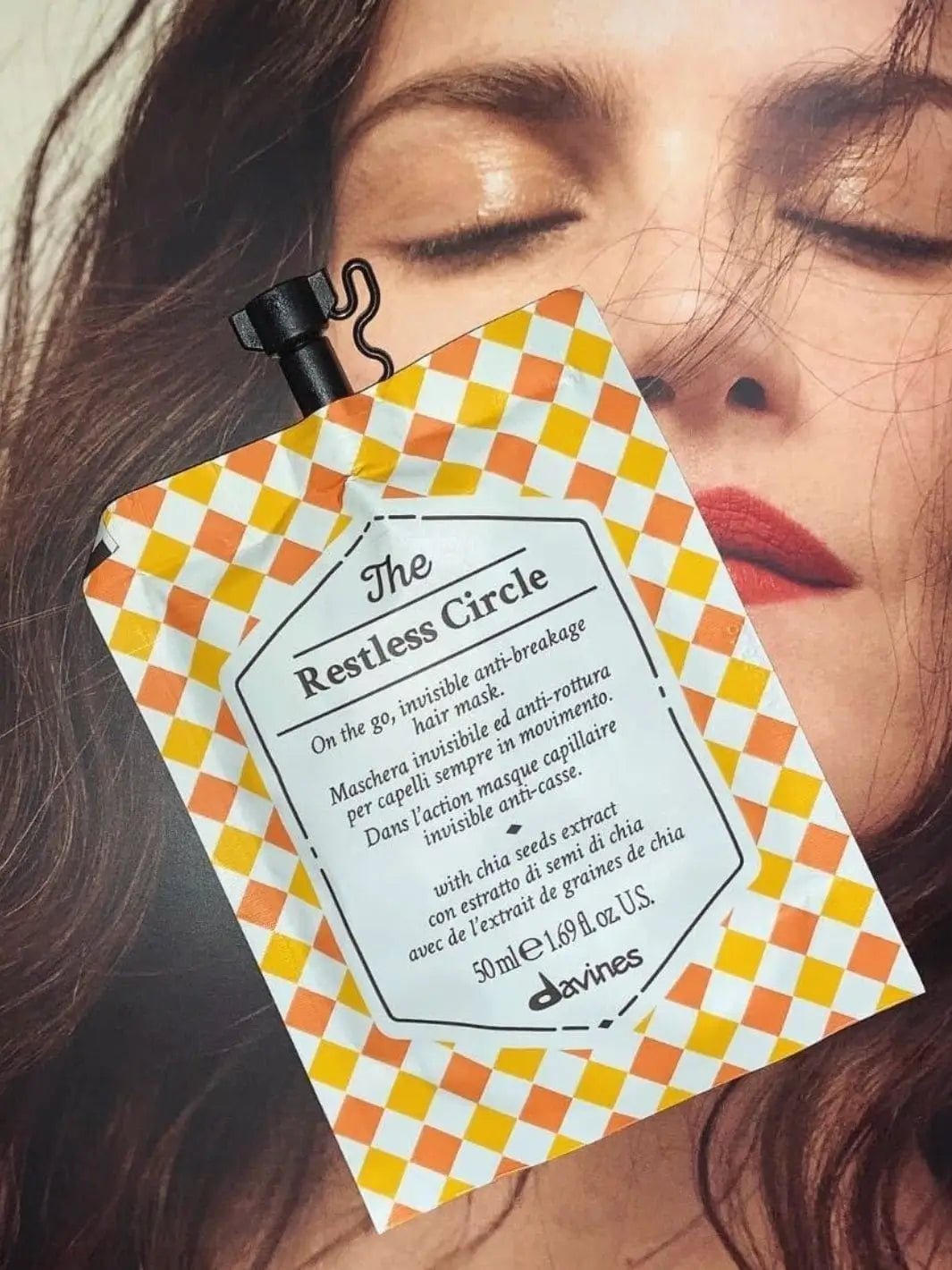 A checkered pouch of Davines The Restless Circle of Chronicles Hair Mask is placed over a close-up photograph of a woman's face | Twentyseven Toronto