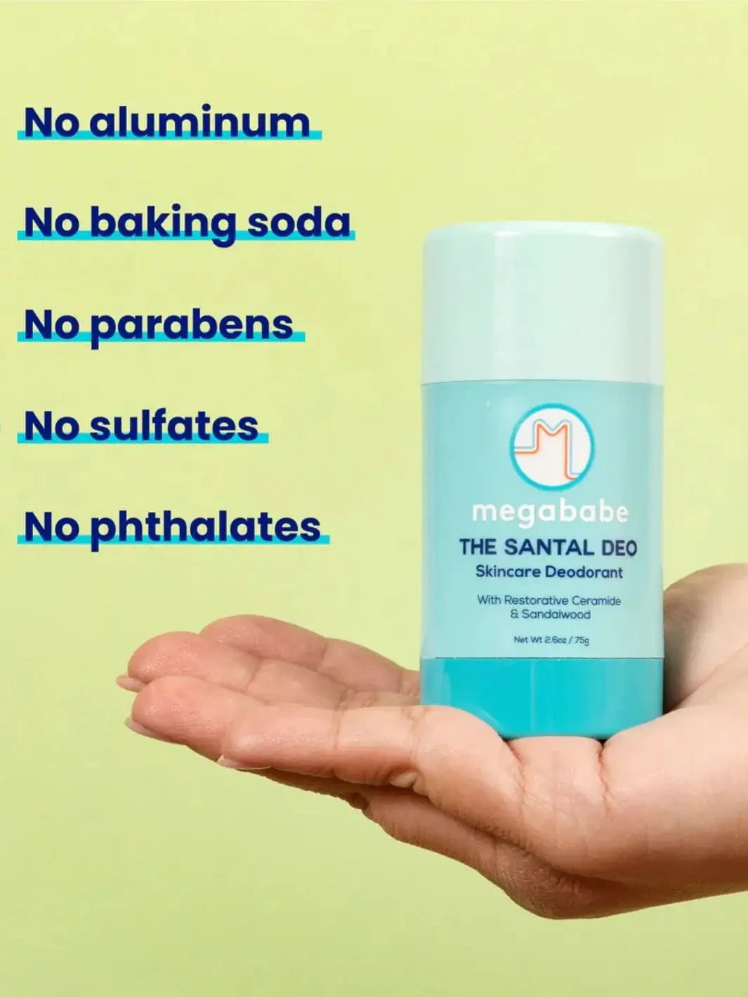 A hand holds a light blue deodorant container against a soft green background alongside a list of ingredient exclusions for Megababe The Santal Deo | Twentyseven Toronto