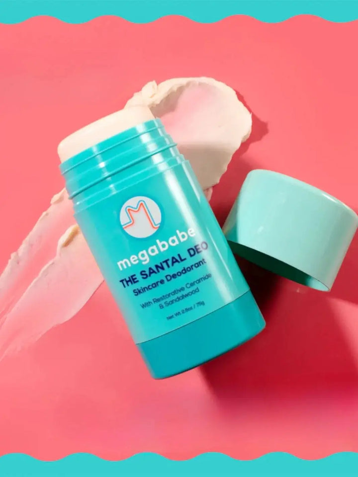 An opened light blue deodorant stick rests on a pink surface next to a smooth swipe of cream, demonstrating the texture of Megababe The Santal Deo | Twentyseven Toronto