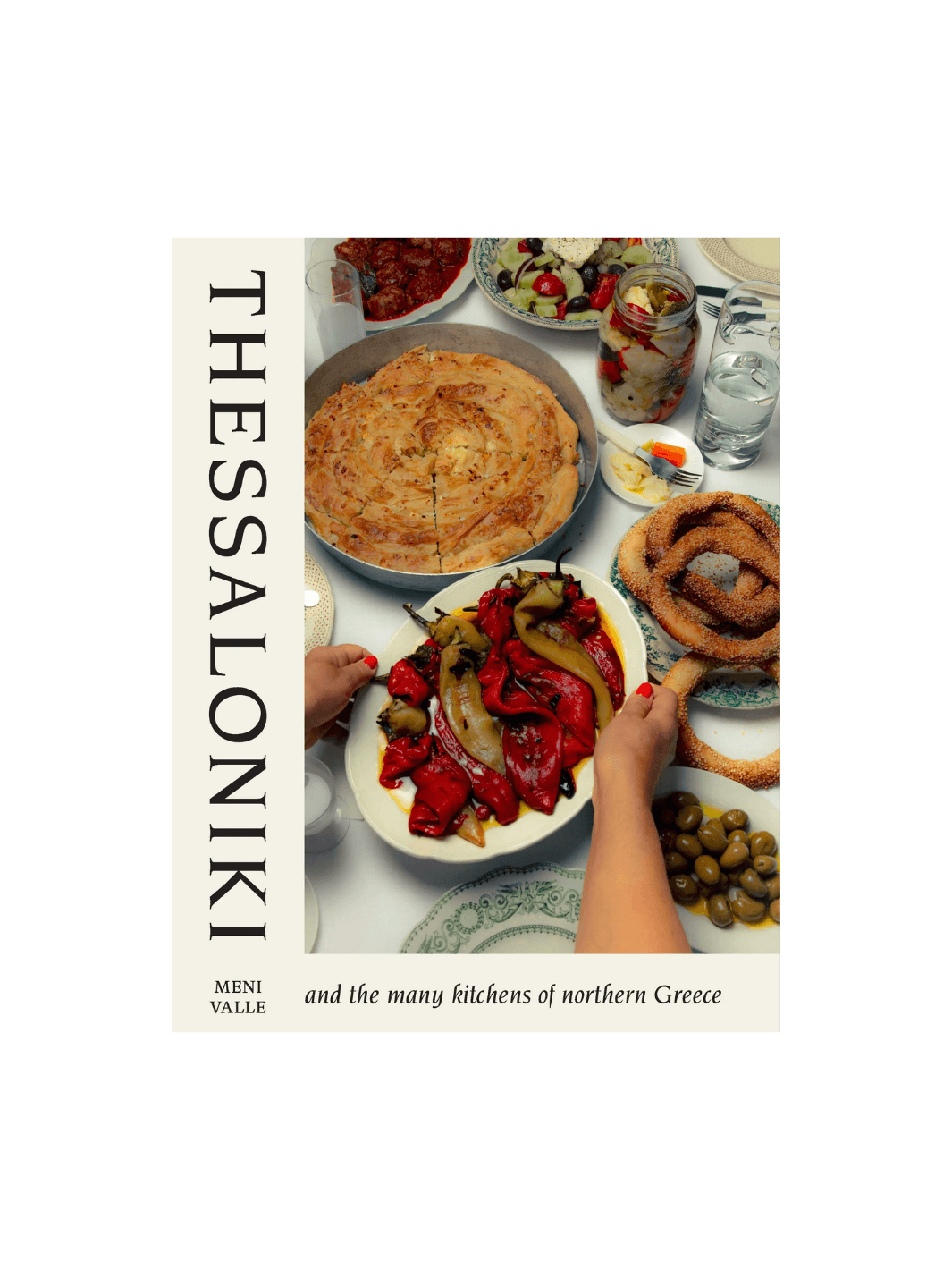 Front cover of the cookbook Thessaloniki: And the Many Kitchens of Northern Greece by Meni Valle, showing a table laden with traditional Greek dishes including roasted red peppers, a large savory pie (pita), olives, and sesame-crusted bread rings (koulouri) | Twentyseven Toronto