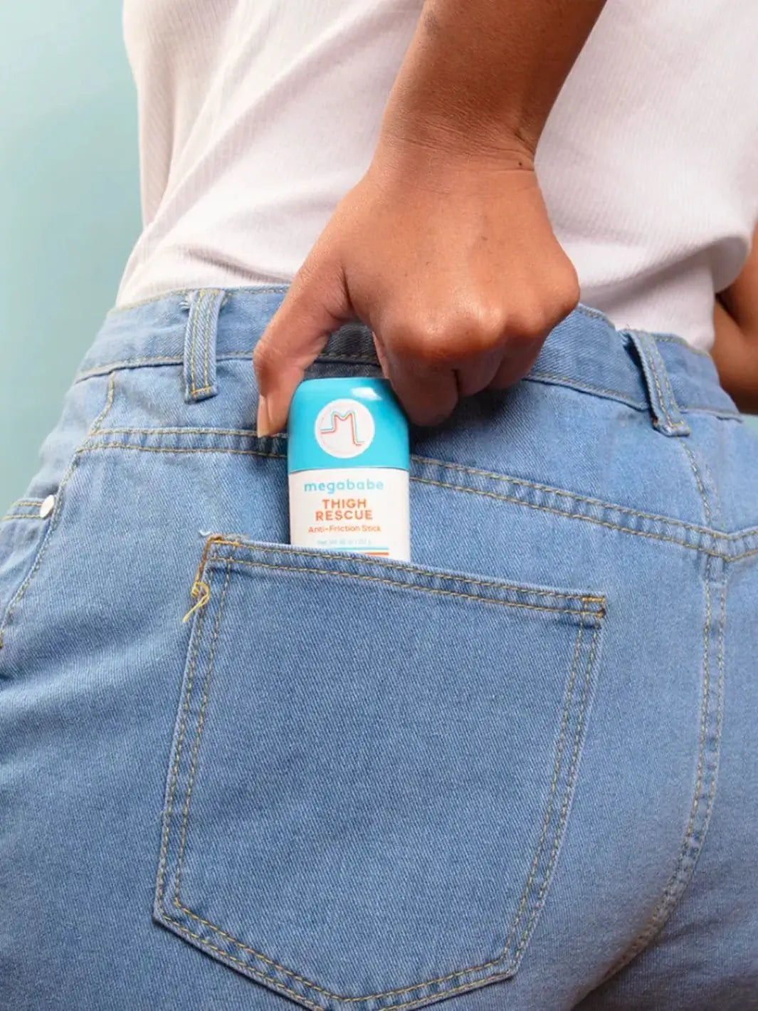 A hand slides a Megababe Thigh Rescue Mini anti-friction stick into the back pocket of a pair of blue jeans to highlight how easily it fits on the go | Twentyseven Toronto