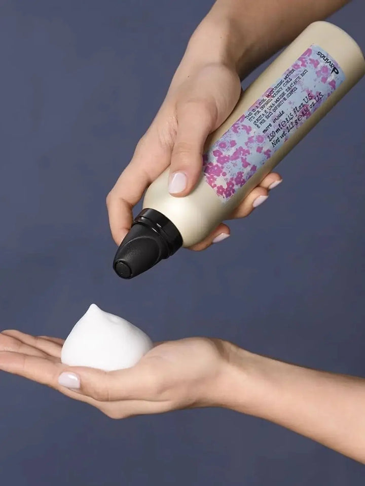 A pair of hands holds a gold aerosol can of Davines This is a Curl Moisturizing Mousse over an open palm holding a dollop of white styling foam | Twentyseven Toronto