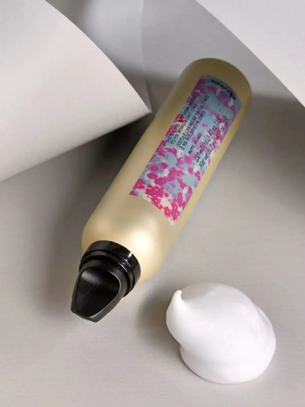 A gold aerosol can of Davines This is a Curl Moisturizing Mousse lies flat next to a pristine mound of white foam on a neutral grey surface | Twentyseven Toronto