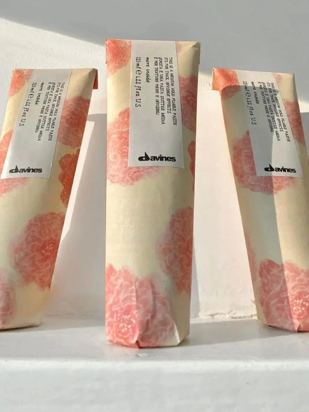 Three tubes of Davines This is a Medium Hold Pliable Paste wrapped in matching pink floral paper stand in a row against a white backdrop | Twentyseven Toronto