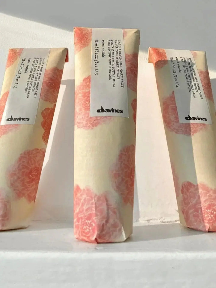 Three tubes of Davines This is a Medium Hold Pliable Paste wrapped in matching pink floral paper stand in a row against a white backdrop | Twentyseven Toronto