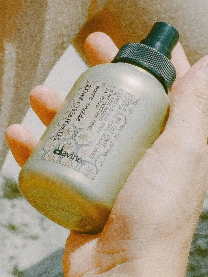 An close-up shot shows a hand holding a compact, travel-sized bottle of Davines This is a Sea Salt Spray | Twentyseven Toronto