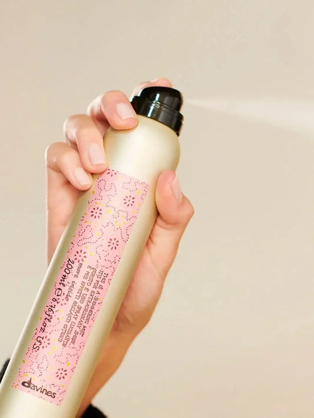 A hand holds a gold aerosol can of Davines This is a Shimmering Mist and presses the nozzle, releasing a fine, light spray | Twentyseven Toronto