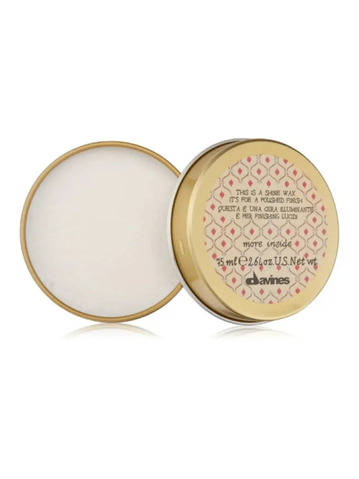 An open gold metal tin of Davines This is a Shine Wax rests on a reflective white surface, displaying the white wax product inside next to its red and gold patterned lid | Twentyseven Toronto