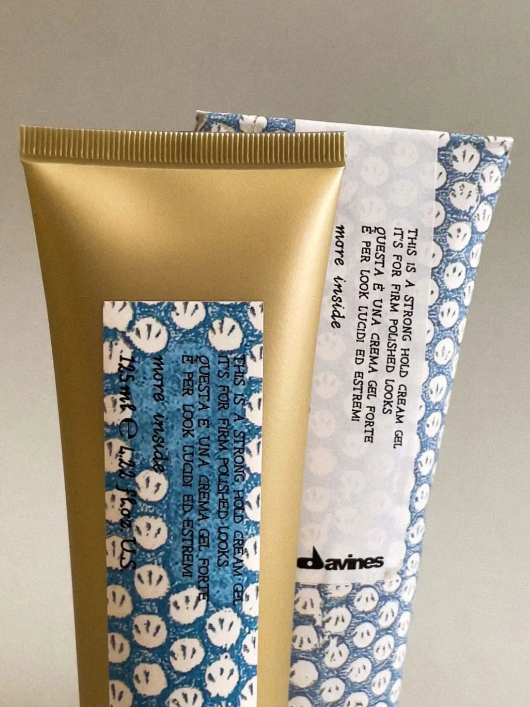A gold tube of Davines This is a Strong Hold Cream Gel stands in front of its matching blue and white patterned paper wrapping | Twentyseven Toronto