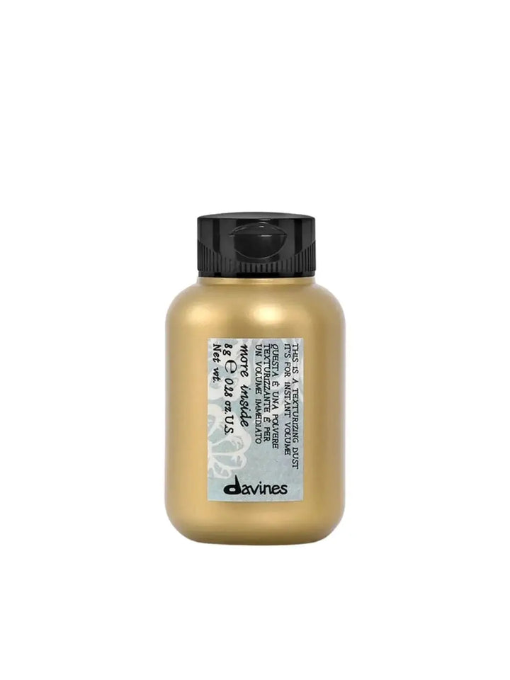 A small, gold plastic bottle of Davines This is a Texturizing Dust with a grey patterned label is centered against a solid white background | Twentyseven Toronto