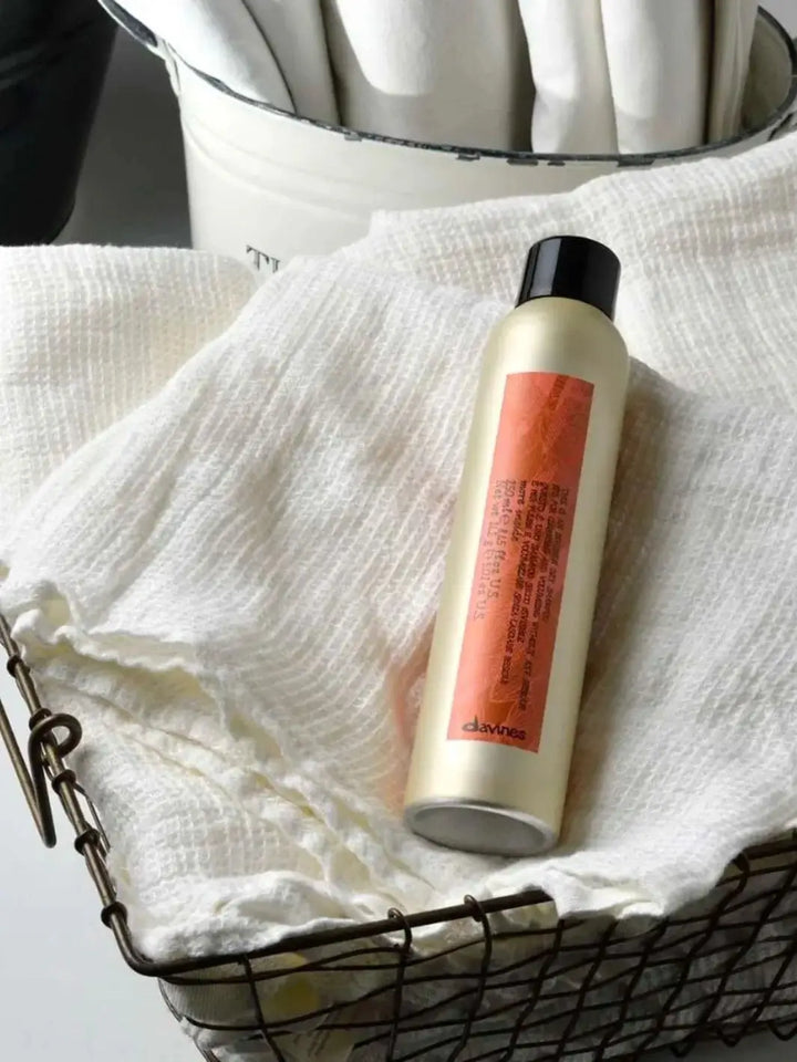 An aerosol can of Davines This is an Invisible Dry Shampoo with a distinctive orange label rests inside a wire basket lined with textured white cloth | Twentyseven Toronto