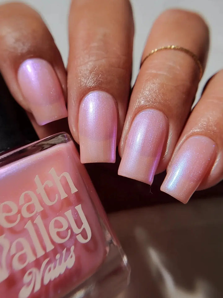A close-up view of square-shaped nails and a matching bottle of Death Valley Nails Throwing Spaghetti At The Wall Of Your Heart To See What Sticks Nail Polish, highlighting its shifting pink iridescence | Twentyseven Toronto
