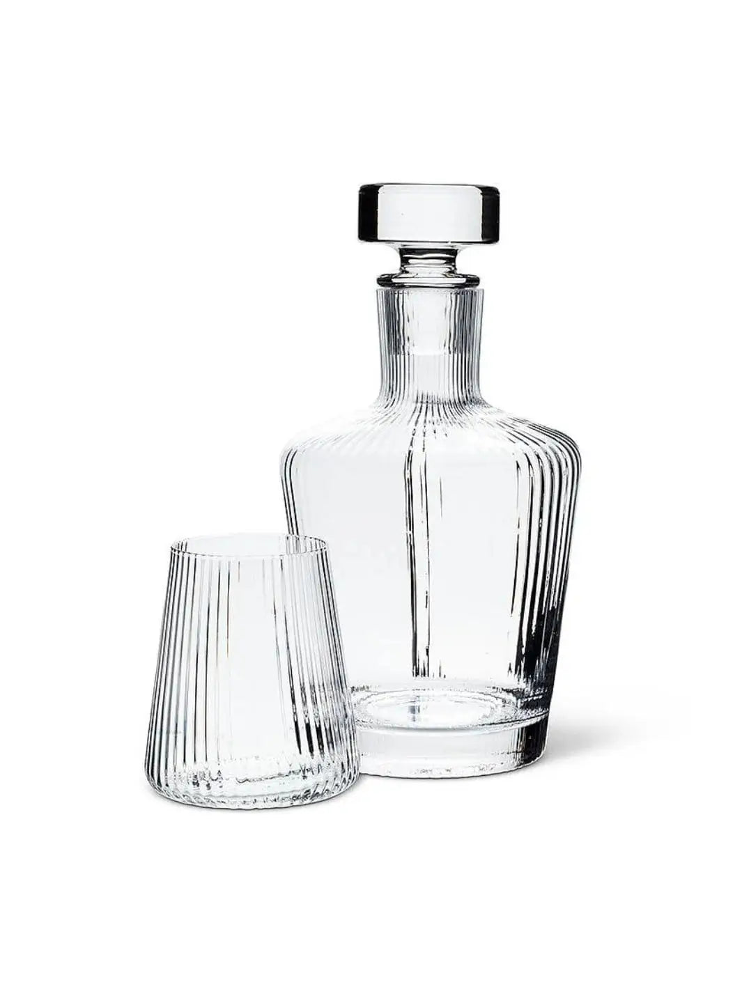 An empty ribbed clear glass Abbott Collection Tight Optic Tumbler is displayed next to a matching glass decanter with a stopper against a solid white background | Twentyseven Toronto