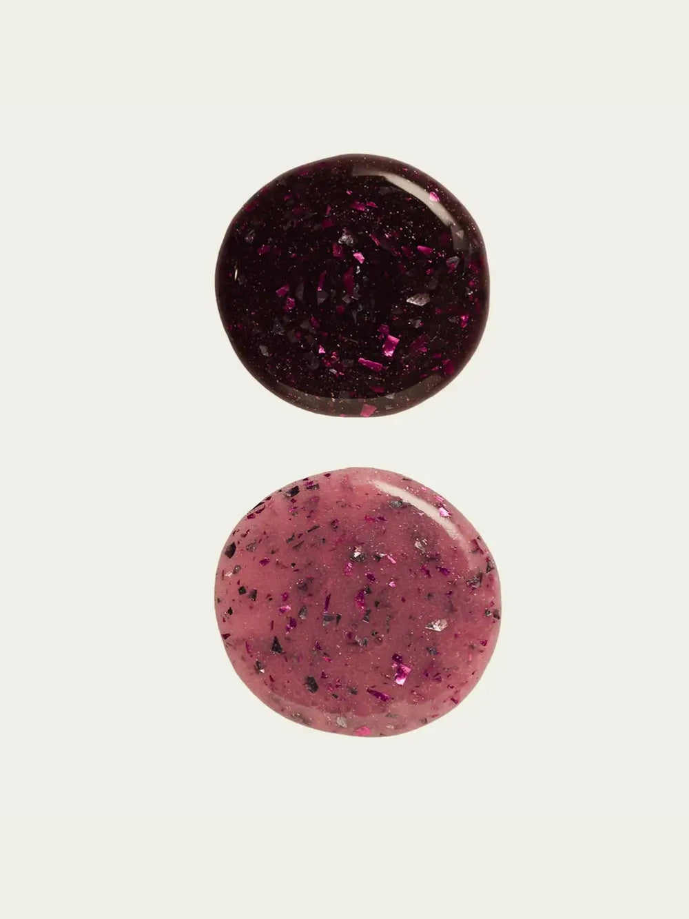 Two circular swatches of glittery 'Till Death Do Us Part' nail polish by Death Valley Nails, one dark red and one pink, on a white background | Twentyseven Toronto