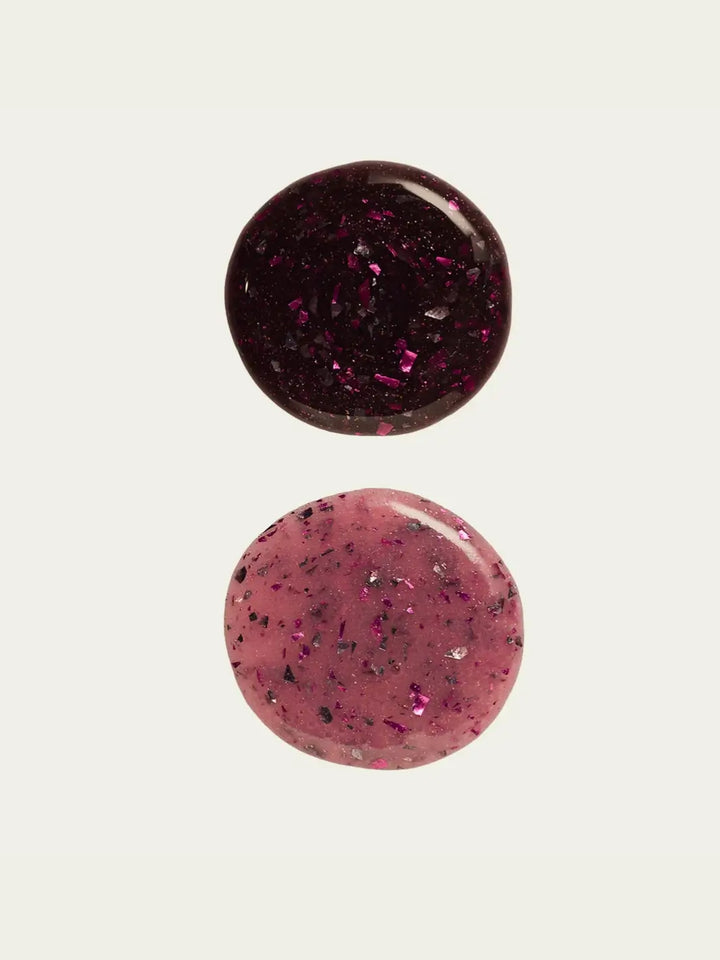 Two circular swatches of glittery 'Till Death Do Us Part' nail polish by Death Valley Nails, one dark red and one pink, on a white background | Twentyseven Toronto