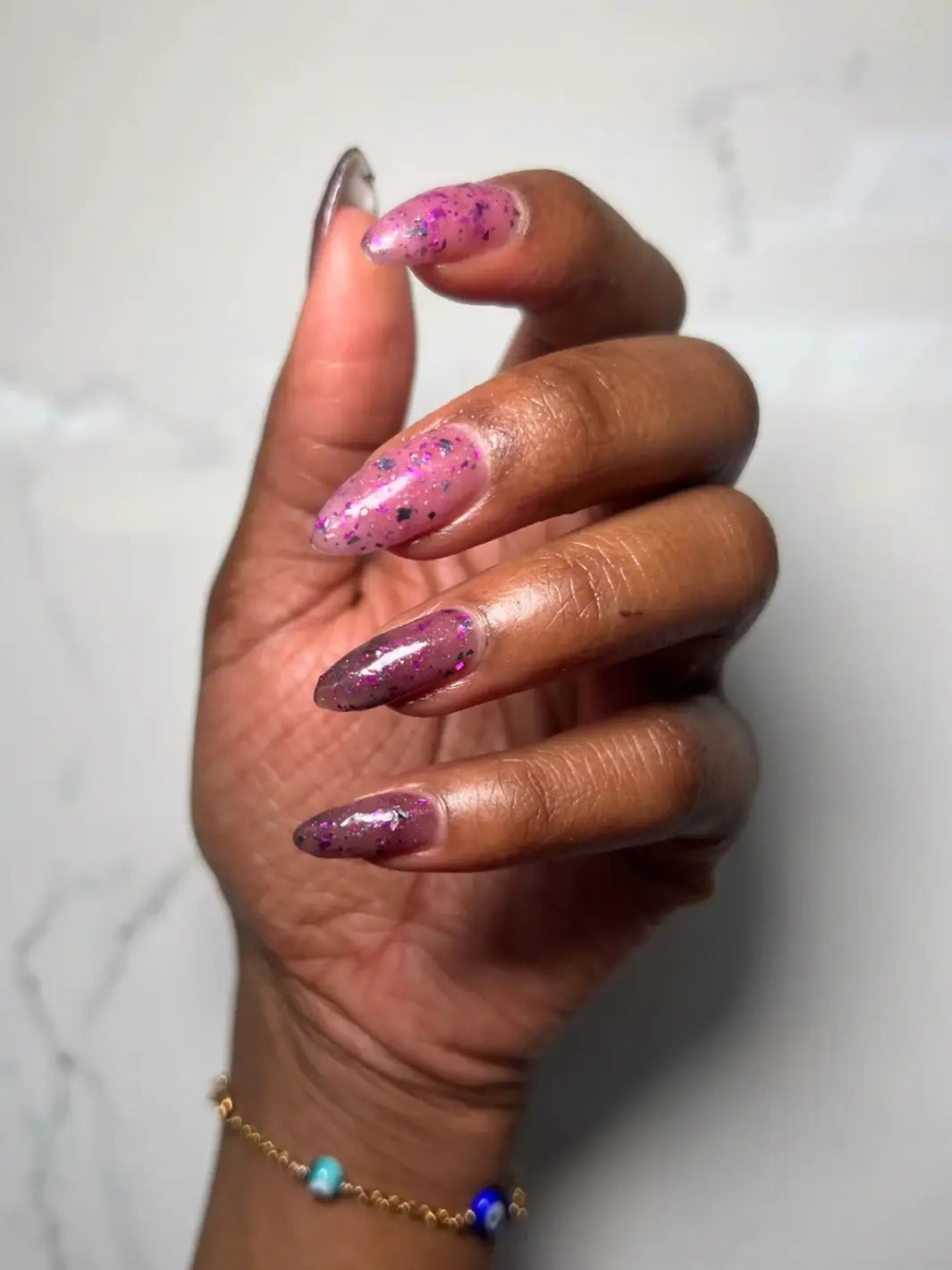 Hand with long glittery pink and purple nails using 'Till Death Do Us Part' nail polish by Death Valley Nails on a marble background | Twentyseven Toronto