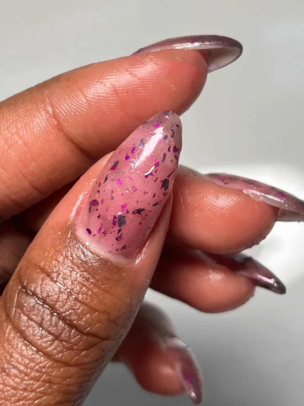 Hand with long glittery pink nails using 'Till Death Do Us Part' nail polish by Death Valley Nails on a white background | Twentyseven Toronto