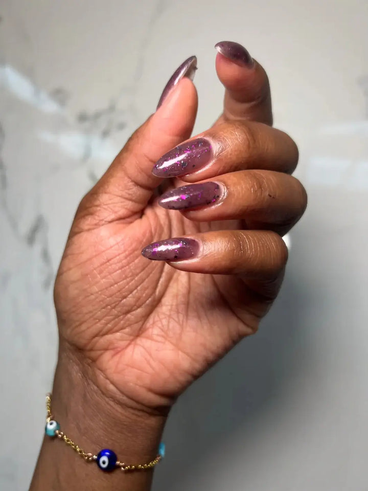 Hand with long glittery purple nails using 'Till Death Do Us Part' nail polish by Death Valley Nails on a marble background | Twentyseven Toronto