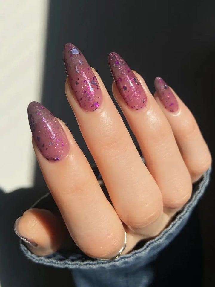 Hand with long glittery pink and purple nails using 'Till Death Do Us Part' nail polish by Death Valley Nails on a marble background | Twentyseven Toronto