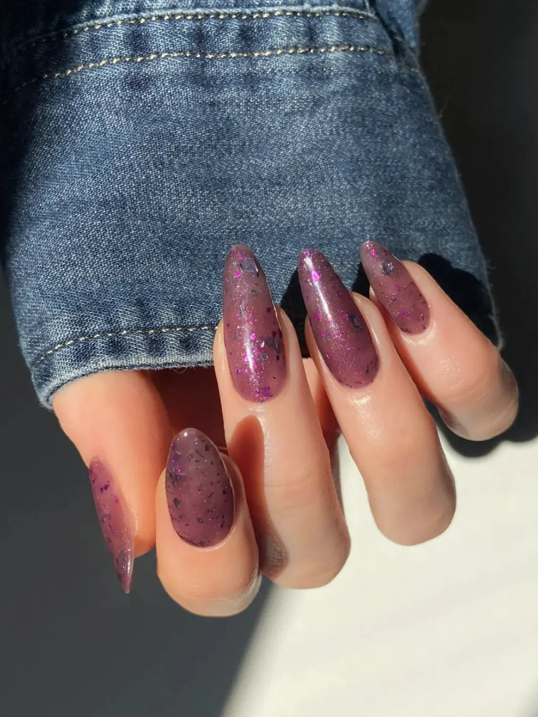 Hand with long glittery pink and purple nails using 'Till Death Do Us Part' nail polish by Death Valley Nails wearing a denim sleeve | Twentyseven Toronto