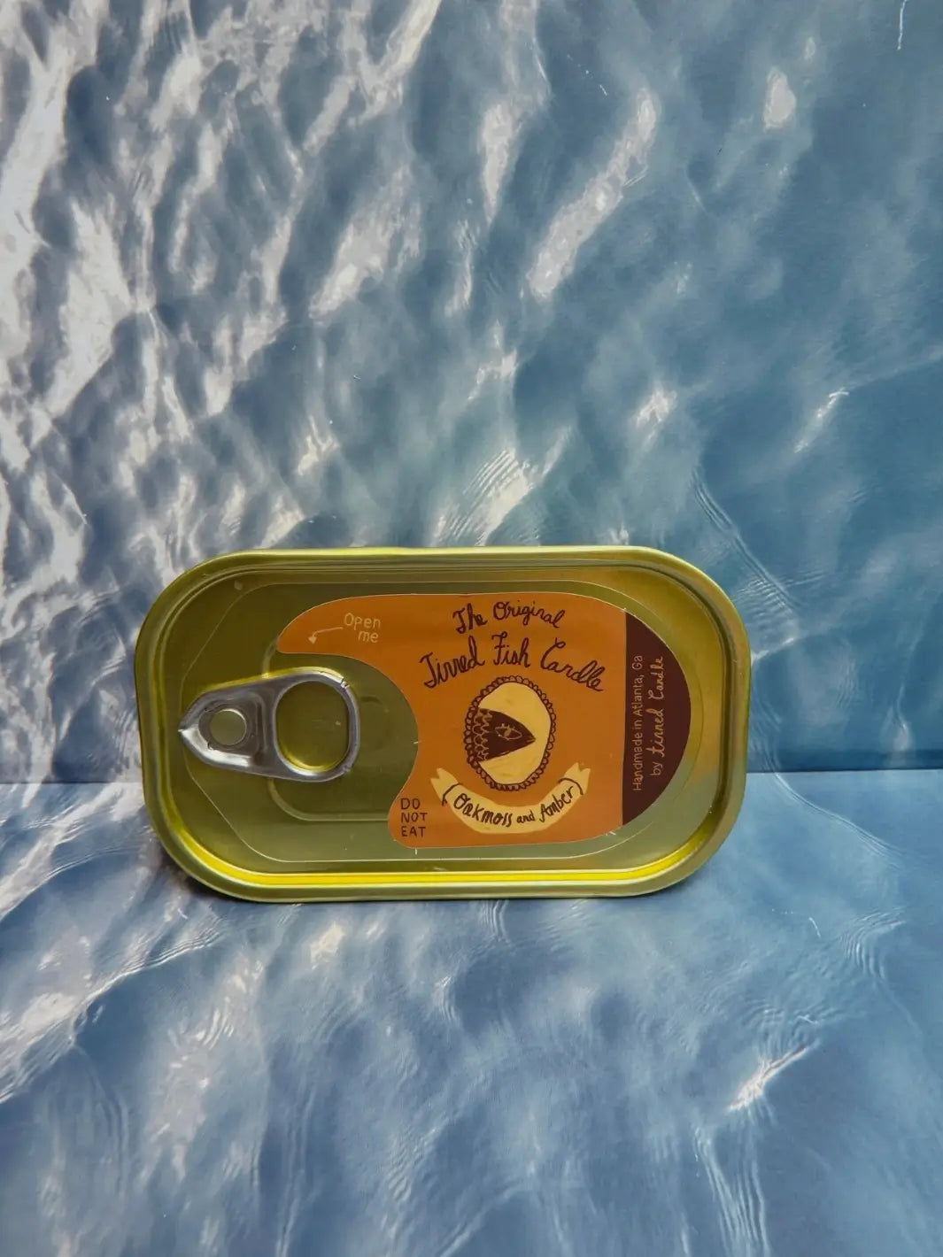 Tin of Tinned Fish Candle with 'Oakmoss and Amber' scent on a blue background | Twentyseven Toronto
