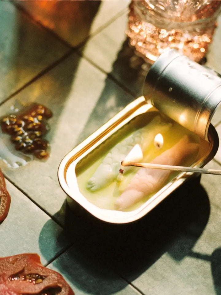 Tinned Fish Candle in Olive Oil Sea Salt being lit with a match on a wooden surface | Twentyseven Toronto