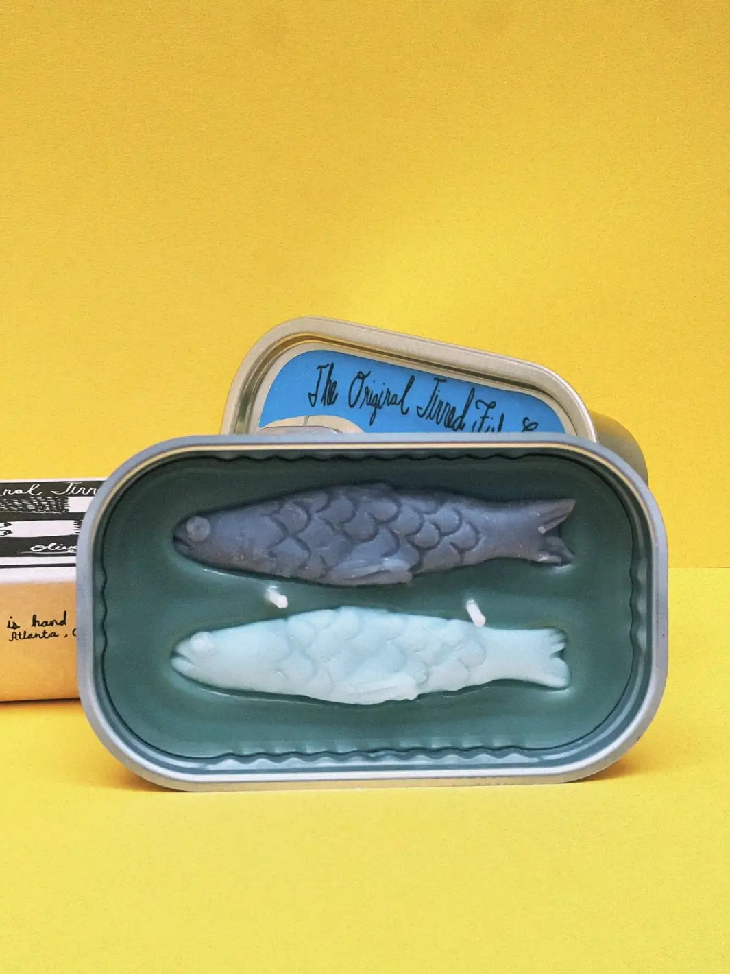Fish-shaped candle in a tin from Tinned Fish Candle on a yellow background | Twentyseven Toronto