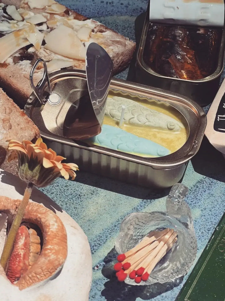 Close-up of a table with various items focusing on the tin fish candle from Tinned Fish Candle | Twentyseven Toronto