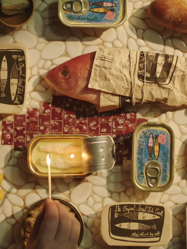 Close-up of Tinned Fish Candle with a lit match on a textured surface | Twentyseven Toronto