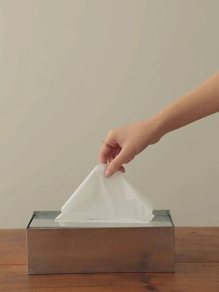 A person’s hand pulls a white tissue from a Fog Linen Work Tissue Box | Twentyseven Toronto