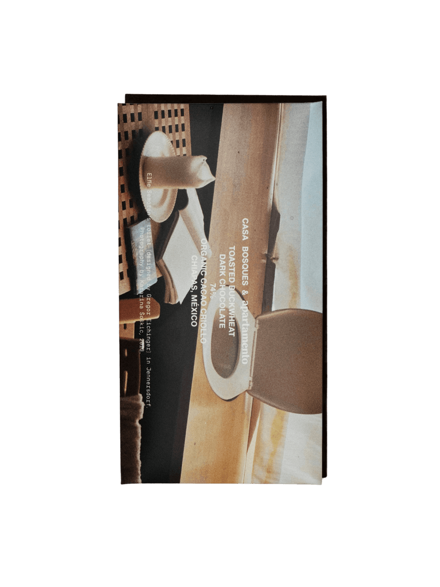 Packaging for the Toasted Buckwheat X Apartmento Chocolate Bar from Casa Bosques features an artistic photograph of a minimalist interior with a lit candle and a wooden chair | Twentyseven Toronto