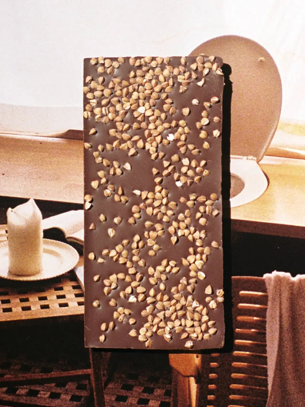 A dark Toasted Buckwheat X Apartmento Chocolate Bar from Casa Bosques is shown from the back, heavily topped with a dense layer of crunchy toasted buckwheat kernels | Twentyseven Toronto