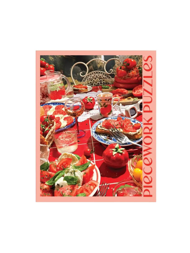 Pink and red jigsaw puzzle packaging featuring a table with food and drinks, labeled 'Piecework Puzzles' | Twentyseven Toronto