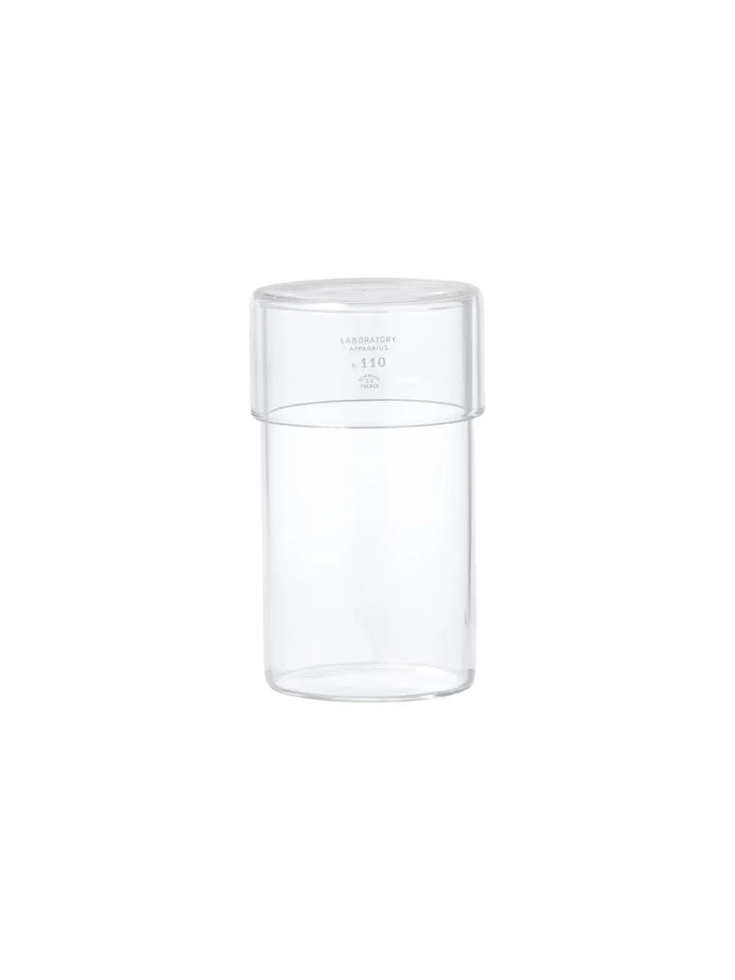 A front-facing product shot of the empty clear glass Tumbler With Lid from Puebco against a stark white backdrop, displaying its minimalist laboratory-inspired branding | Twentyseven Toronto