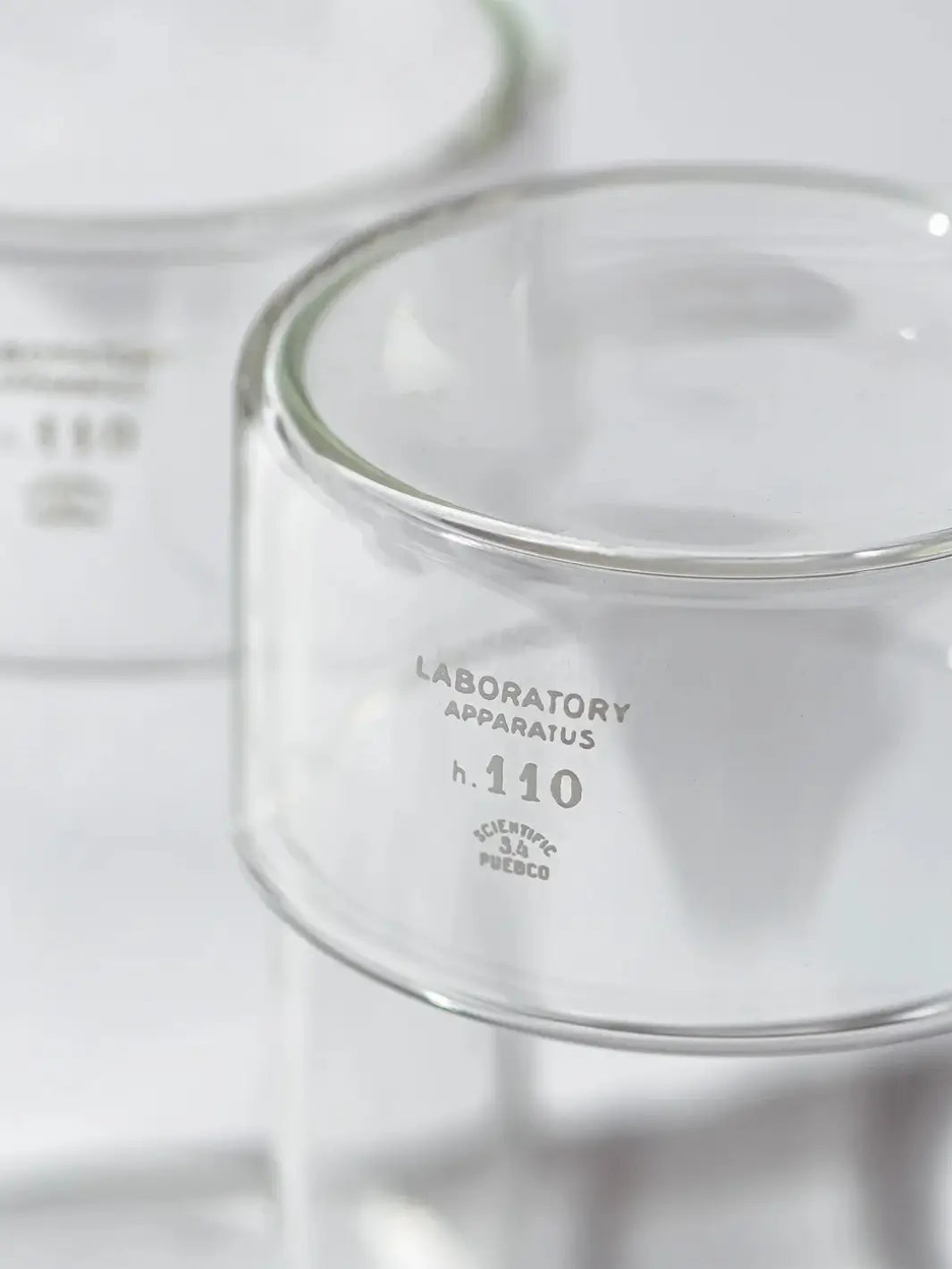 Close-up detail shot focusing on the white printed text on the glass surface of the Tumbler With Lid from Puebco, reading "LABORATORY APPARATUS h. 110 SCIENTIFIC PUEBCO" | Twentyseven Toronto