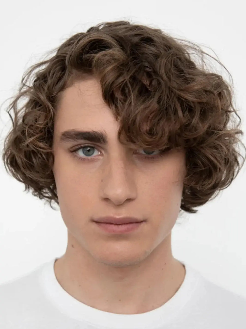 A close-up headshot of a model showcasing soft, textured curls styled using R+Co TURNTABLE Curl Defining Cream | Twentyseven Toronto